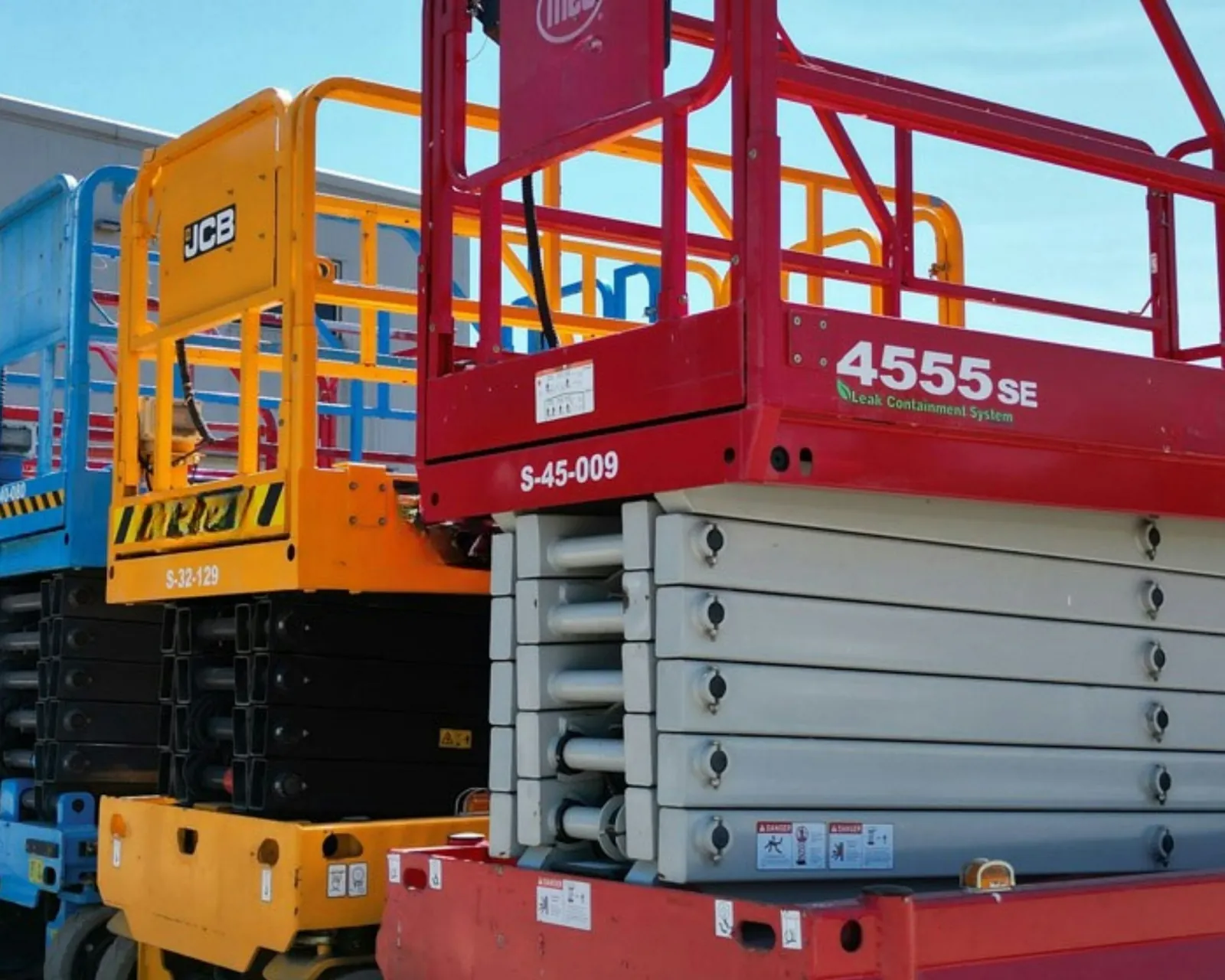 A row of rental scissor lifts parked outside an equipment yard