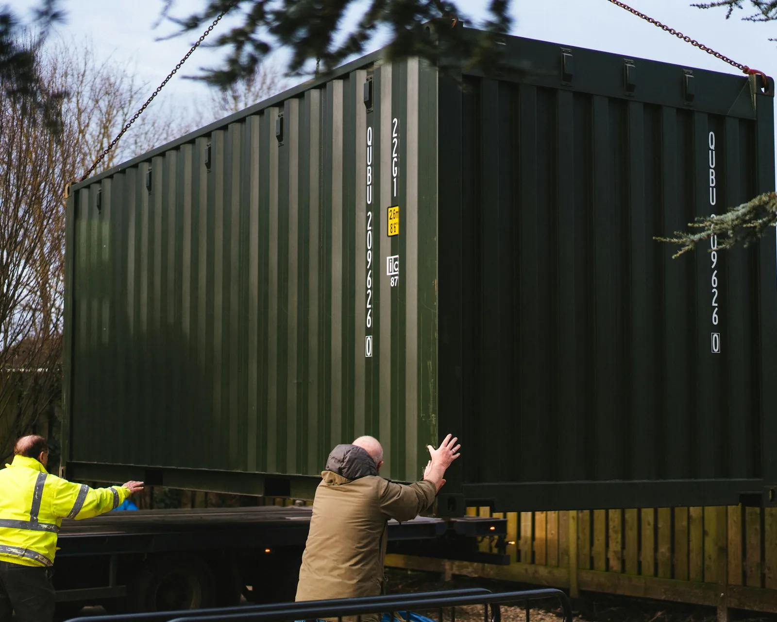 Two workers guiding a storage container into place behind a home